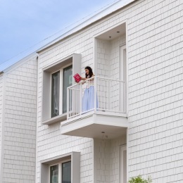 Person on a balcony reading a book with a white building